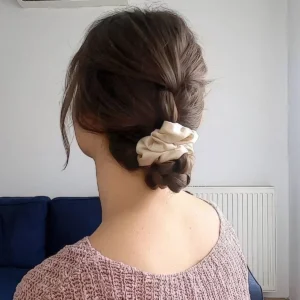 a braided ending up in a low bun with a vanilla colored scrunchie and face framing hair is a lovely hairstyle