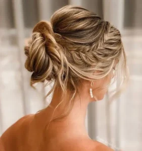 a messy yet chic wedding updo with a loose fishtail braid halo a bump on top a midi messy bun and face framing hair